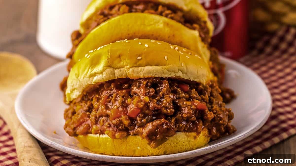 31 Forgotten Grandma Potluck Recipes Worth Bringing Back 20 Three sloppy joe sandwiches filled with seasoned ground beef and diced red peppers on a white plate, placed on a red and white checkered cloth.
