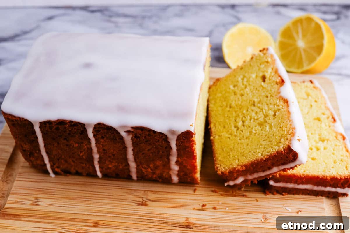 31 Forgotten Grandma Potluck Recipes Worth Bringing Back 33 A lemon loaf cake with glaze on a wooden board with sliced lemons in the background.