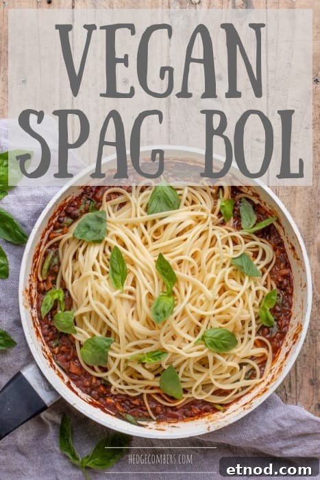 wooden background with white pan with vegan spaghetti bolognese piled up and scattered with fresh basil leaves
