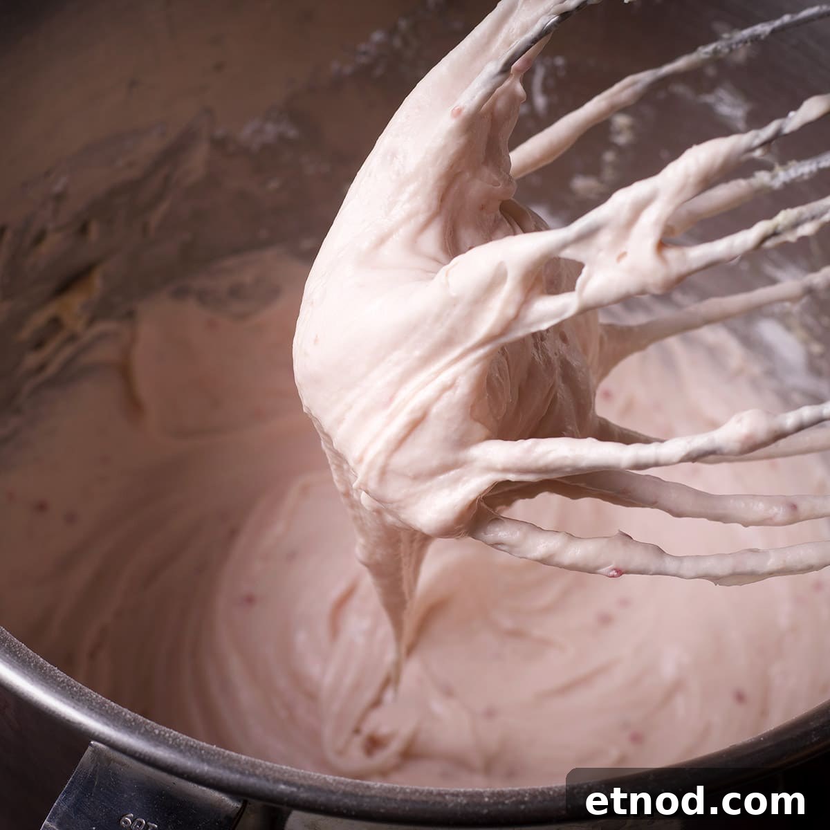 Raspberry Cream Cheese Frosting Recipe for Cakes & Cupcakes 7 Raspberry cream cheese frosting dripping from the whisk attachment of an electric mixer into a mixing bowl.