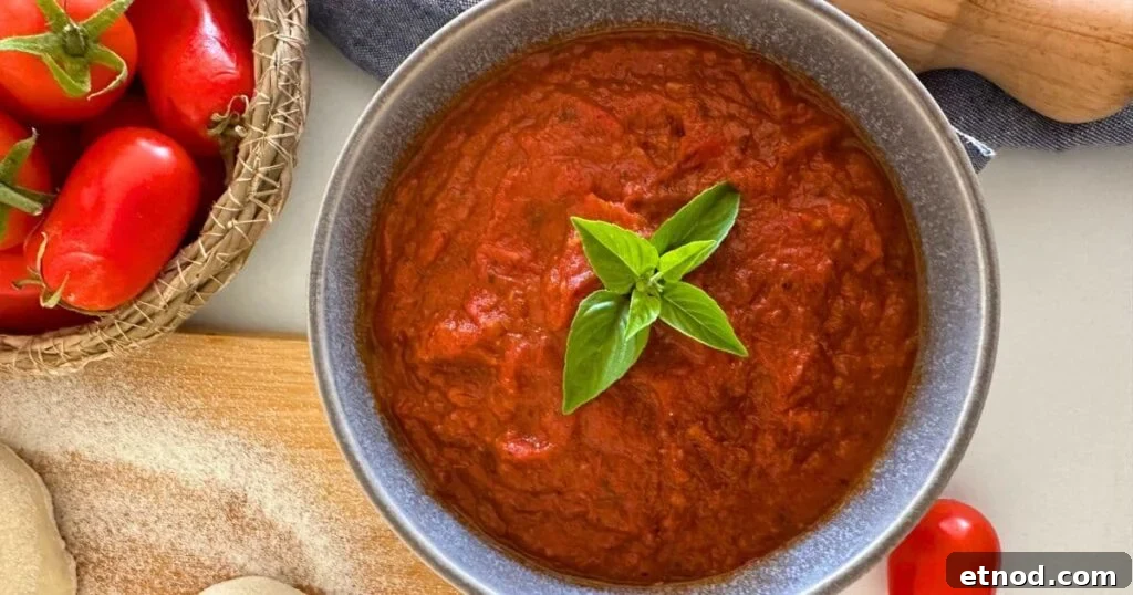 Authentic Homemade Pizza Sauce Recipe for Restaurant-Style Flavor 2 Bowl of homemade pizza sauce ready to be spread on sourdough pizza. There are a few small basil leaves in the centre of the homemade pizza sauce and you can see some fresh tomatoes in a basket to the left of the sauce.