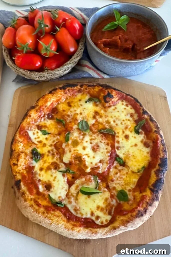 Authentic Homemade Pizza Sauce Recipe for Restaurant-Style Flavor 12 A sourdough pizza that has been topped with homemade pizza sauce displayed on a wooden board. You can also see a bowl of roma tomatoes and a bowl of pizza sauce towards the top of the photo.