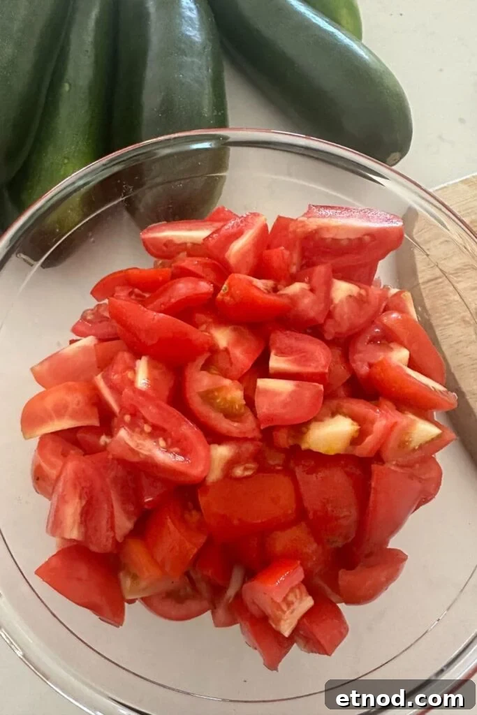 Authentic Homemade Pizza Sauce Recipe for Restaurant-Style Flavor 6 A glass bowl of diced Roma Tomatoes. You can see some whole green zucchini in the background.
