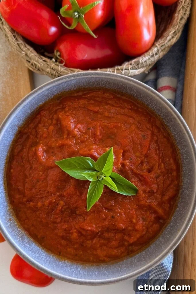 Authentic Homemade Pizza Sauce Recipe for Restaurant-Style Flavor 10 A grey stoneware bowl filled with homemade pizza sauce. There is a piece of green basil in the centre of the sauce for decoration. You can see a bowl of red roma tomatoes at the top of the photos.