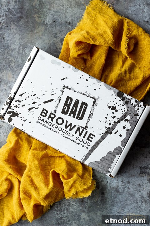 A closed box of Bad Brownie brownies on a yellow linen napkin against a grey backdrop.