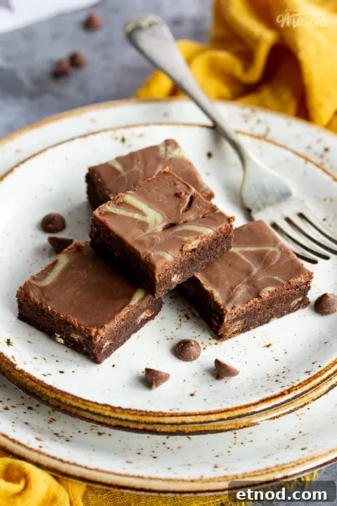 4 chocolate orange brownies in a stack on top of 3 stacked plates with a fork. Set on a yellow linen napkin over a grey background, there's also scattered chocolate chips and a Bad Brownie box in the background.