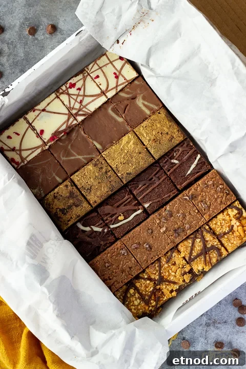 An open box of Bad Brownie brownies revealing all 6 flavours on a yellow linen napkin against a grey backdrop with chocolate chips scattered around.