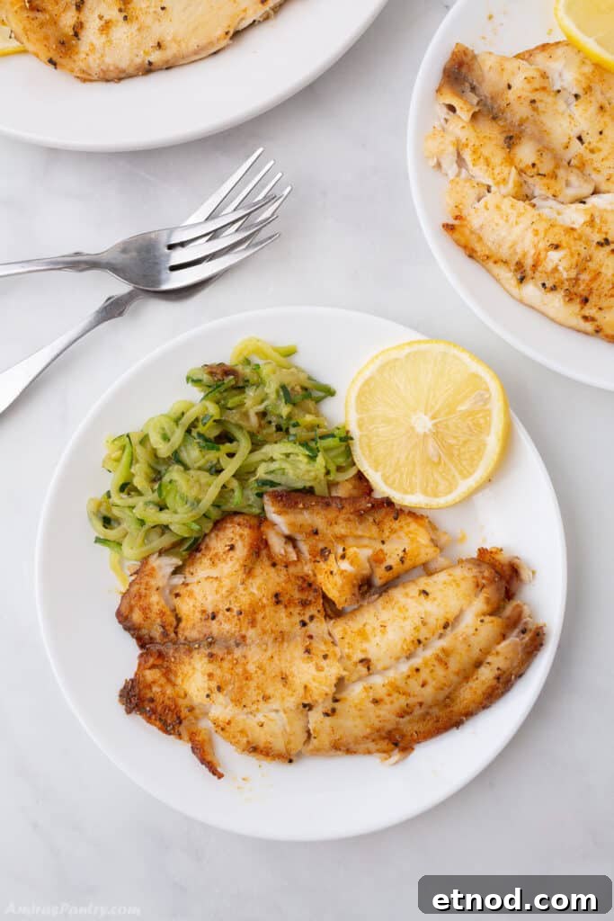 A bird's eye view of a plate with tilapia and some veggies and forks on the side.