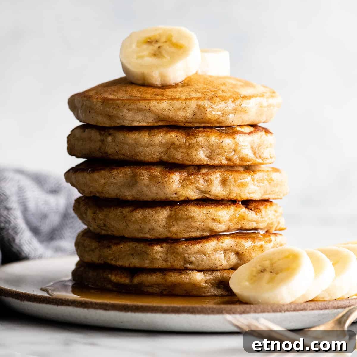 Served banana pancakes front view of a stack of 6 banana pancakes with syrup and sliced bananas