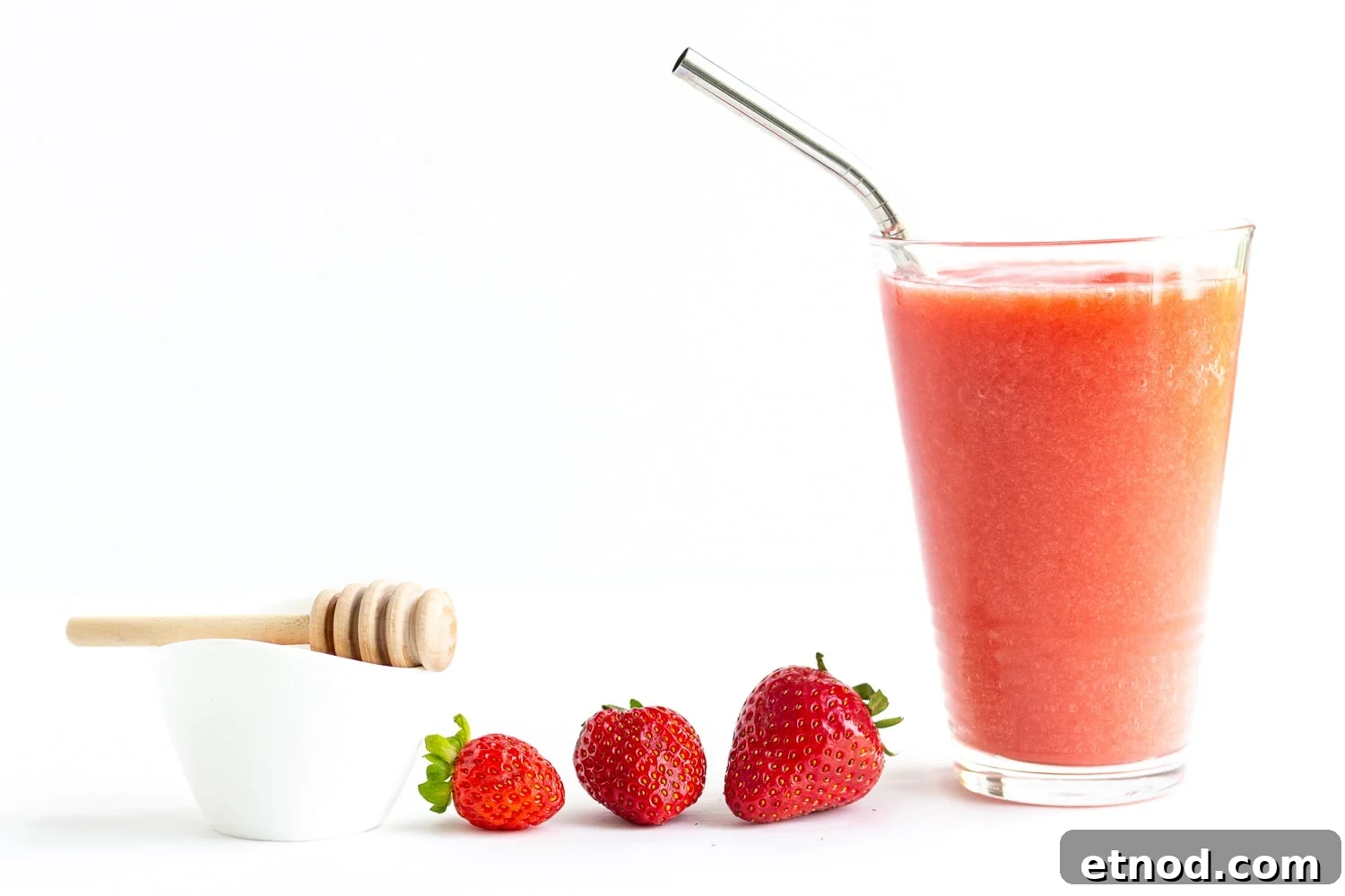Refreshing Strawberry Slush Recipe for Summer Sips 3 Small white bowl of honey with honey dipper, three strawberries and tall glass of strawberry slushie.