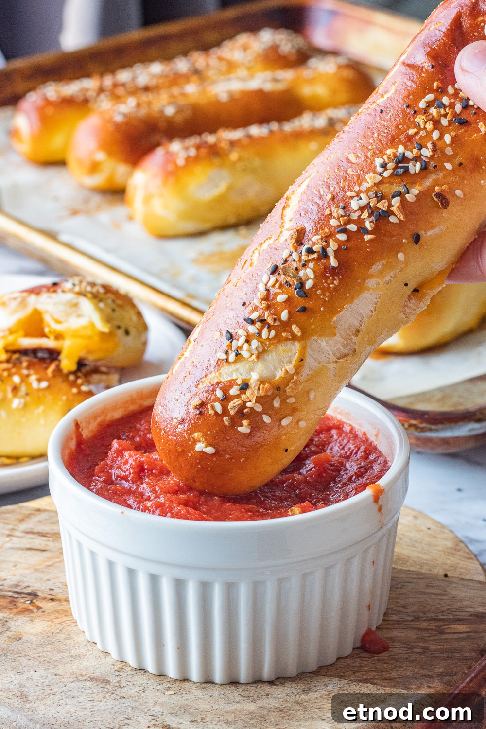 Easy Cheese Pretzels made with homemade soft pretzel dough, stuffed with cheddar cheese and crunchy seasonings on top. Baked cheese pretzel above tomato sauce in white bowl.