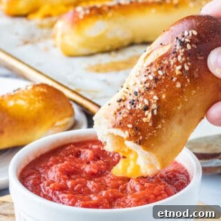 Baked cheese pretzel above white bowl of pizza sauce.