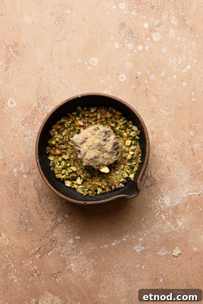 A bowl with chopped pistachio and a cookie dough ball.