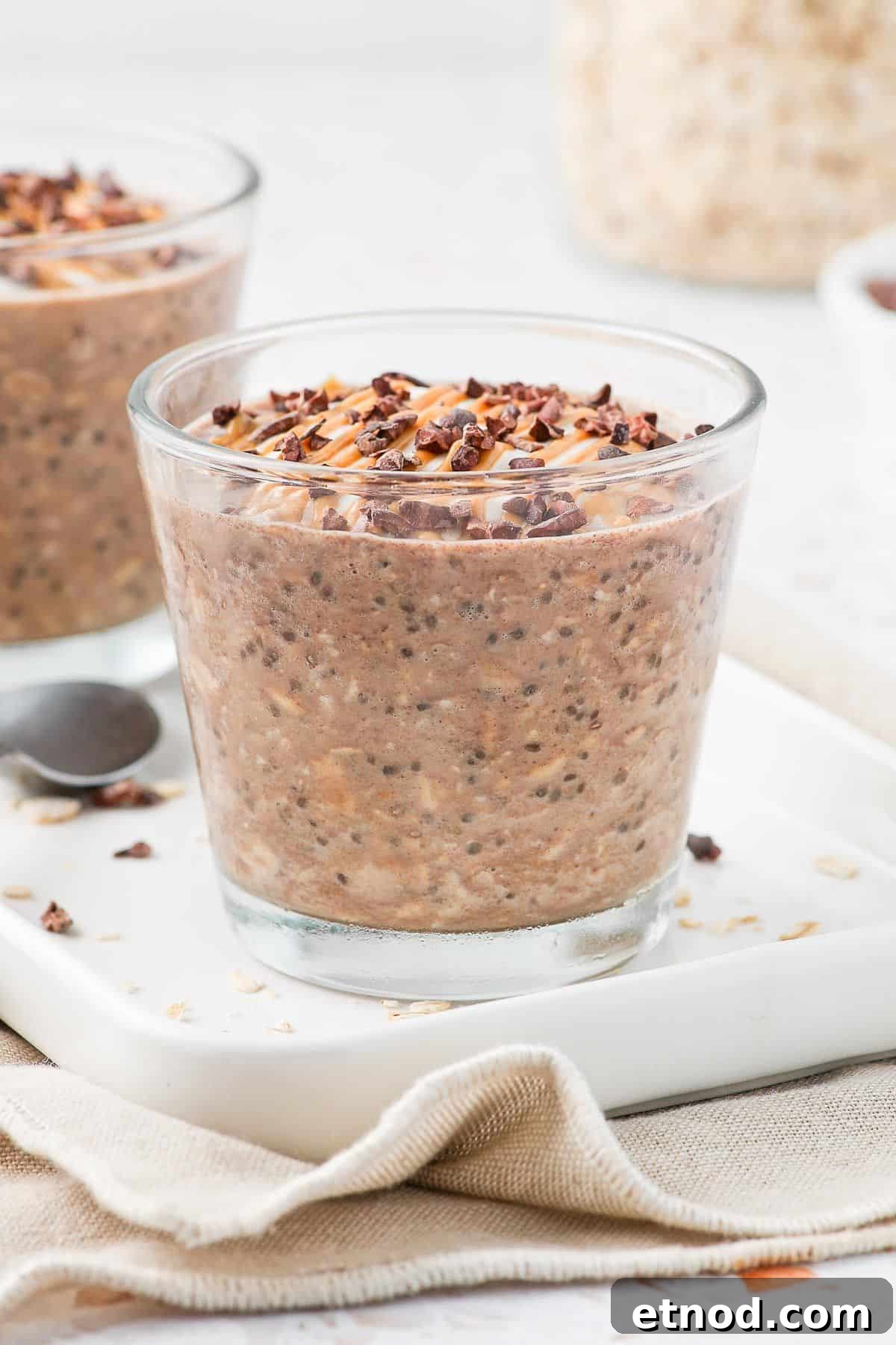 Jar of overnight oats, sitting on a white plate, garnished with peanut butter and cacao nibs.