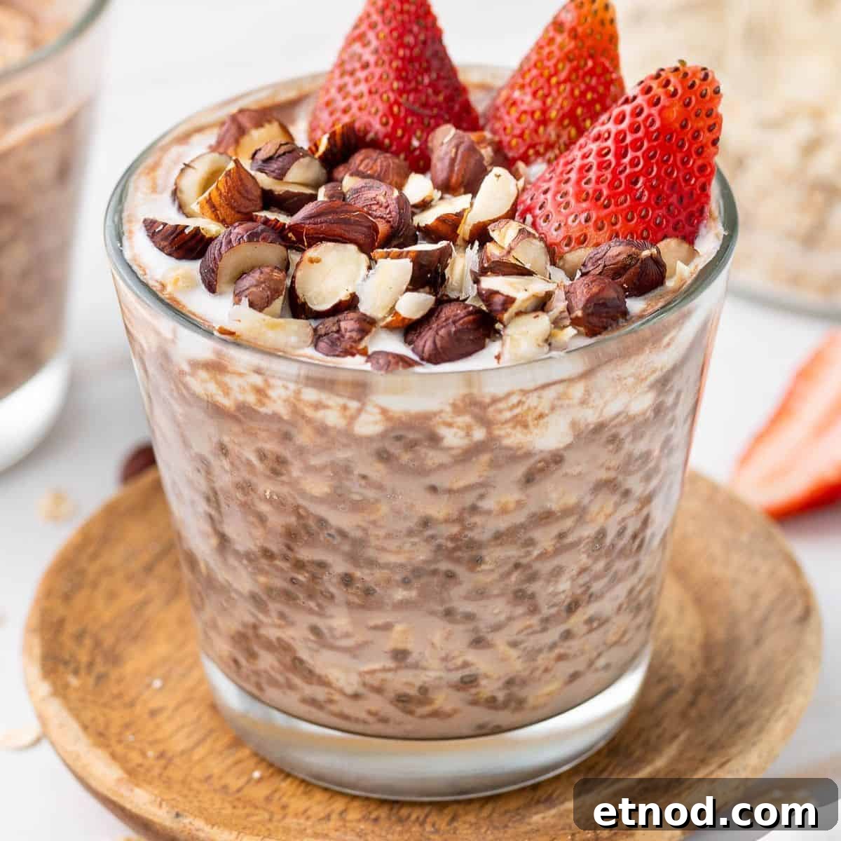 Glass jar of overnight oats, topped with yoghurt, crushed hazelnuts and cut strawberries.