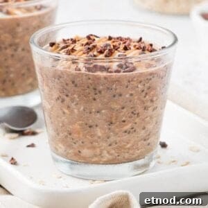Jar of overnight oats, sitting on a white plate, garnished with peanut butter and cacao nibs.