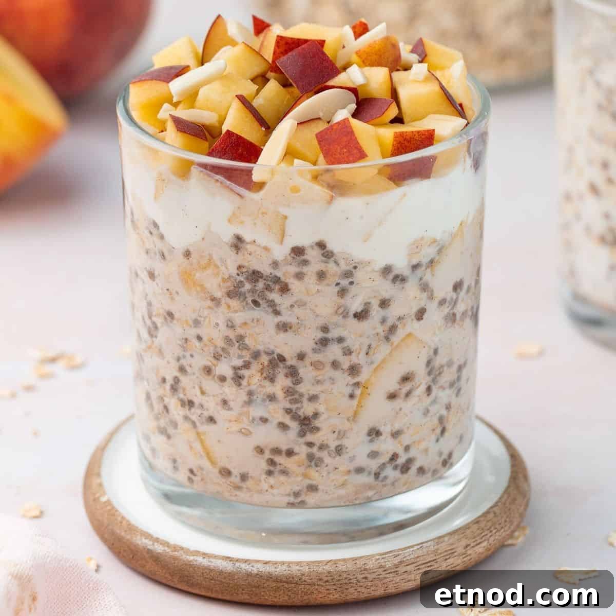 Glass jar of overnight oats topped with yoghurt, cubes of fresh peach and flaked almonds.