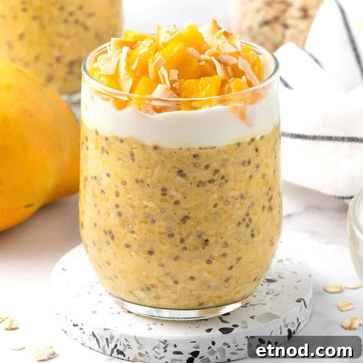 Glass jar of mango overnight oats, topped with yoghurt, mango pieces and flaked coconut.