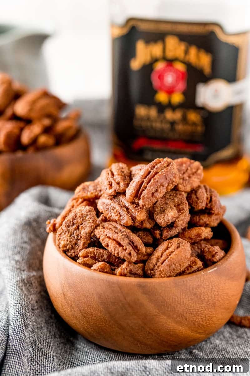 Candied Pecans made in a crockpot are an addictive party treat! With a delicious maple bourbon coating, they’re a great edible gift too! crockpot candied pecans in a wooden bowl in front of a bottle of jim beam black