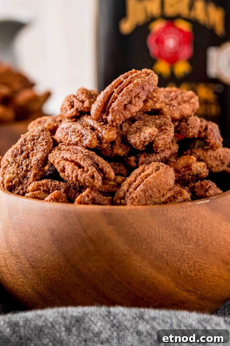 Candied Pecans made in a crockpot are an addictive party treat! With a delicious maple bourbon coating, they’re a great edible gift too! close up of candied pecans in a wooden bowl