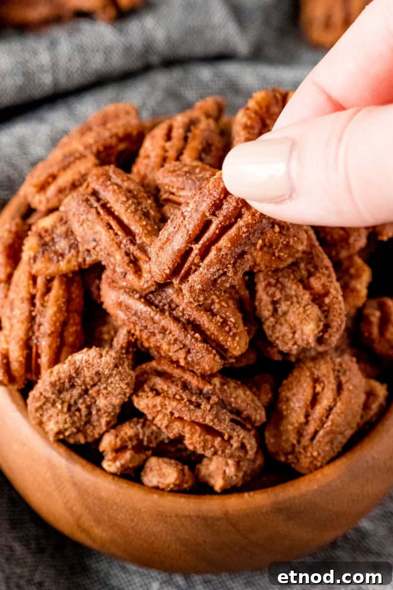 Candied Pecans made in a crockpot are an addictive party treat! With a delicious maple bourbon coating, they’re a great edible gift too! fingers taking candied pecan from a bwol
