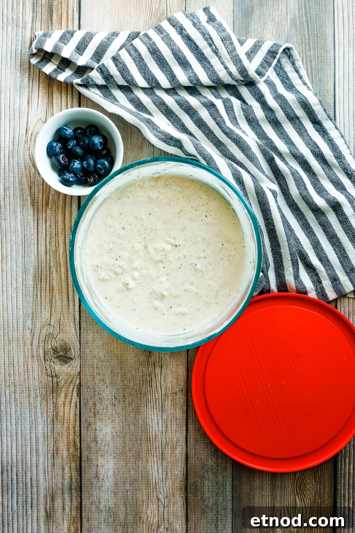 High-Protein Overnight Oats Recipe for Muscle Gain and Meal Prep 4 a bowl of blueberries next to a bowl of oats and a red plastic lid.
