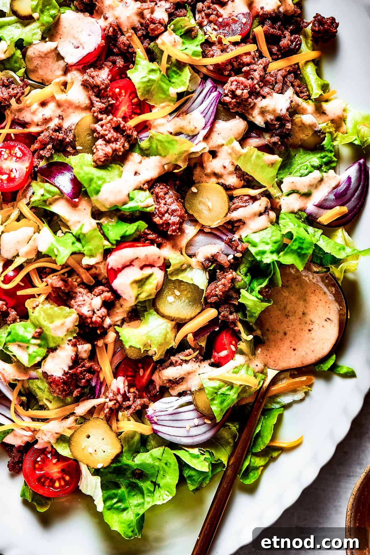 This Big Mac Salad brings all the classic flavors you love but with a healthier twist. It's a guilt-free way to satisfy your burger cravings. Close-up of a Big Mac Salad with red onion, ground beef, shredded cheese, and more.
