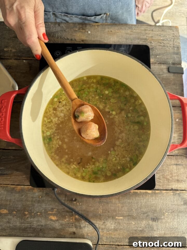 Healing Ginger Chicken Soup Recipe for Cold Relief 8 meatballs on a wooden spoon above the chicken soup in a dutch oven