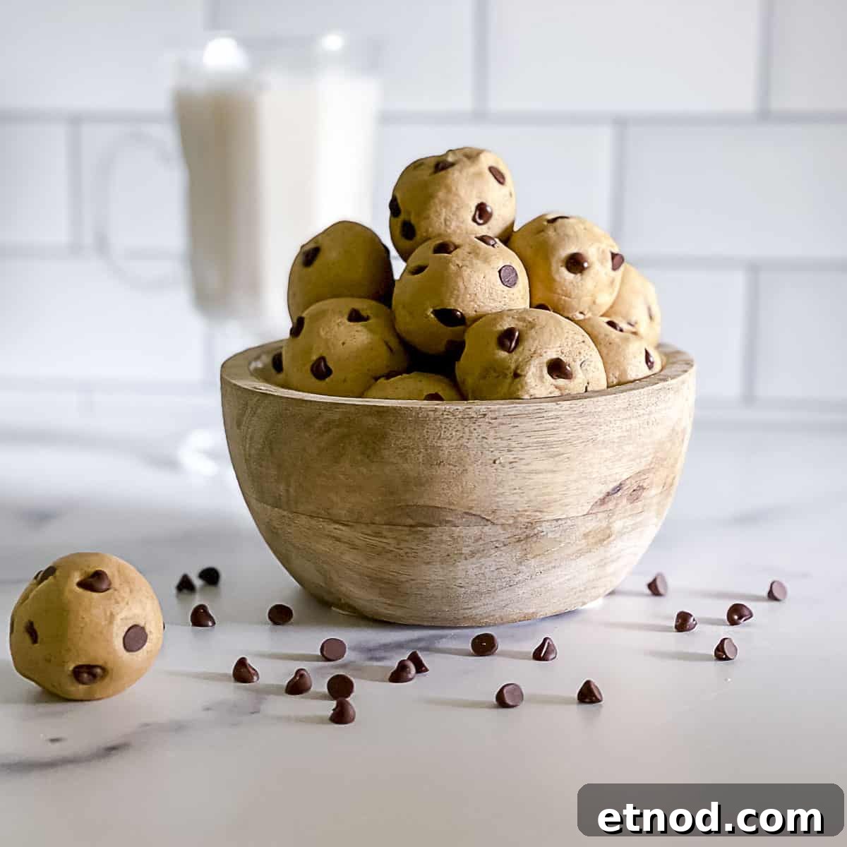 Edible no bake chocolate chip cookie dough balls stacked in a bowl with chips sprinkled on table.