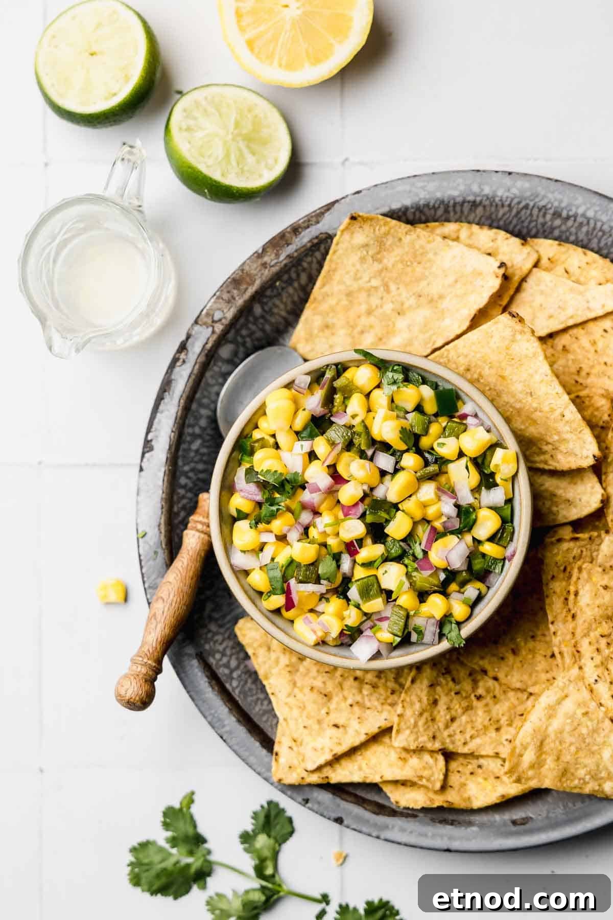 Roasted chili corn salsa in small bowl next to tortilla chips and cilantro.