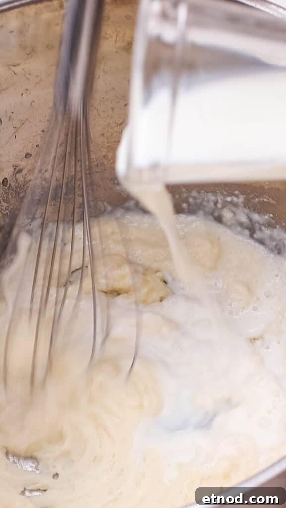 Adding milk to butter and flour mixture in saucepan.