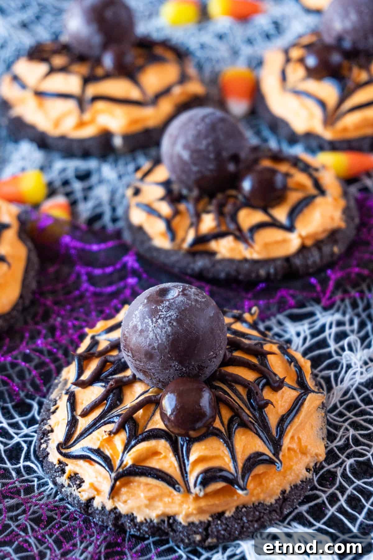 Halloween Spider Cookies decorated with Lindor chocolate, chocolate-covered blueberry, sitting on a black and orange frosted cookie, on a white and purple netting background.