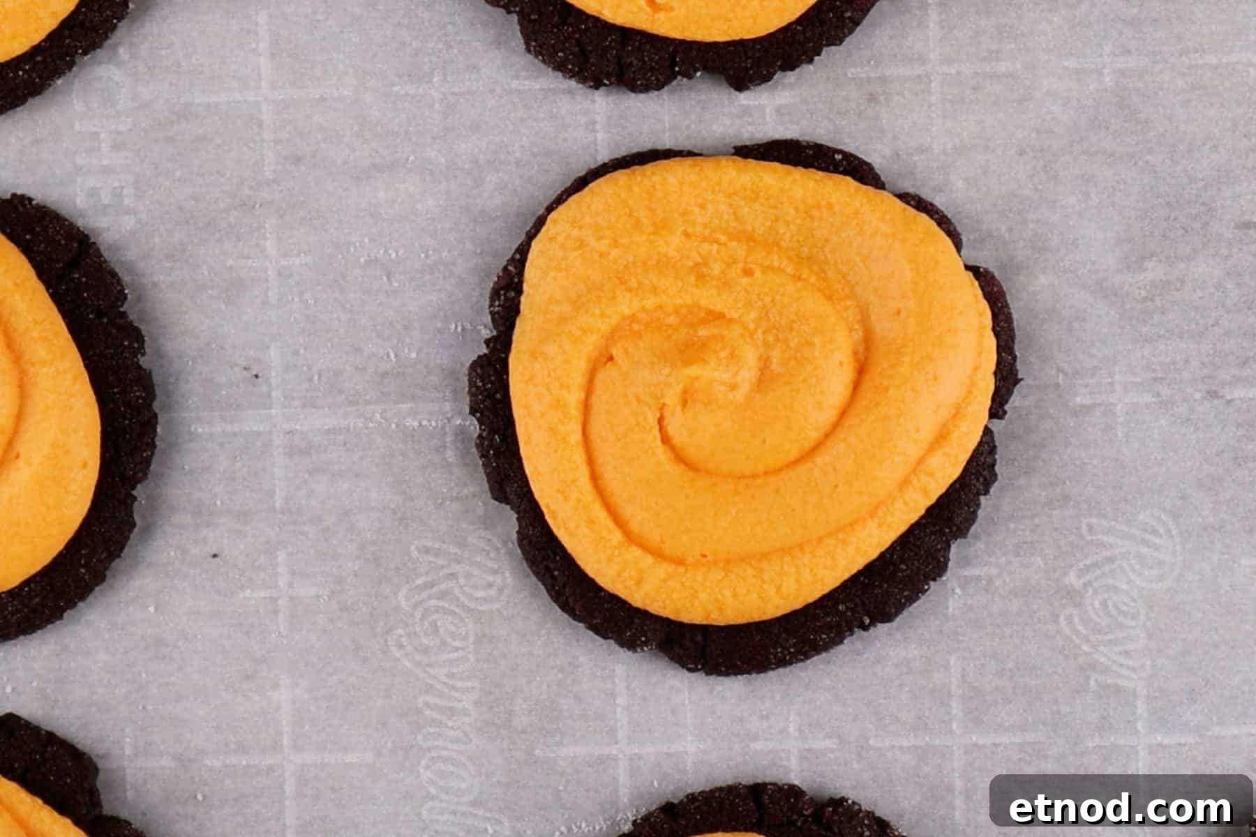 Orange colored buttercream piped on top of a chocolate sugar cookie.