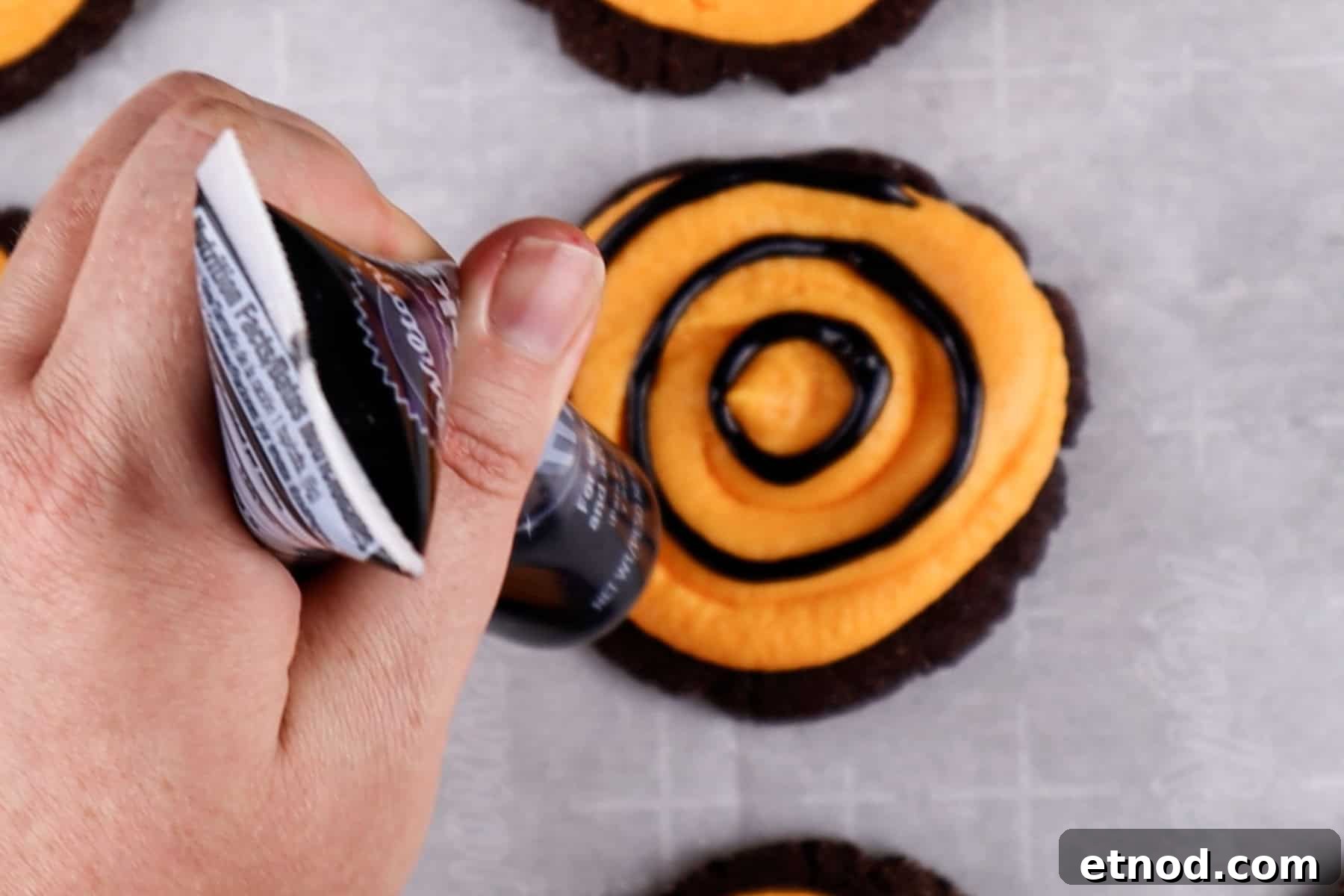 Piping concentric circles of black gel onto a cookie frosted with orange frosting.