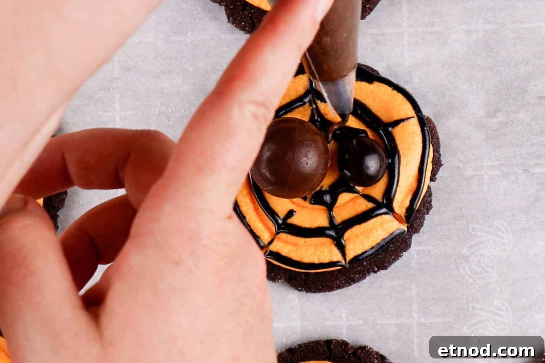 Using chocolate frosting to pipe on legs to the spider.