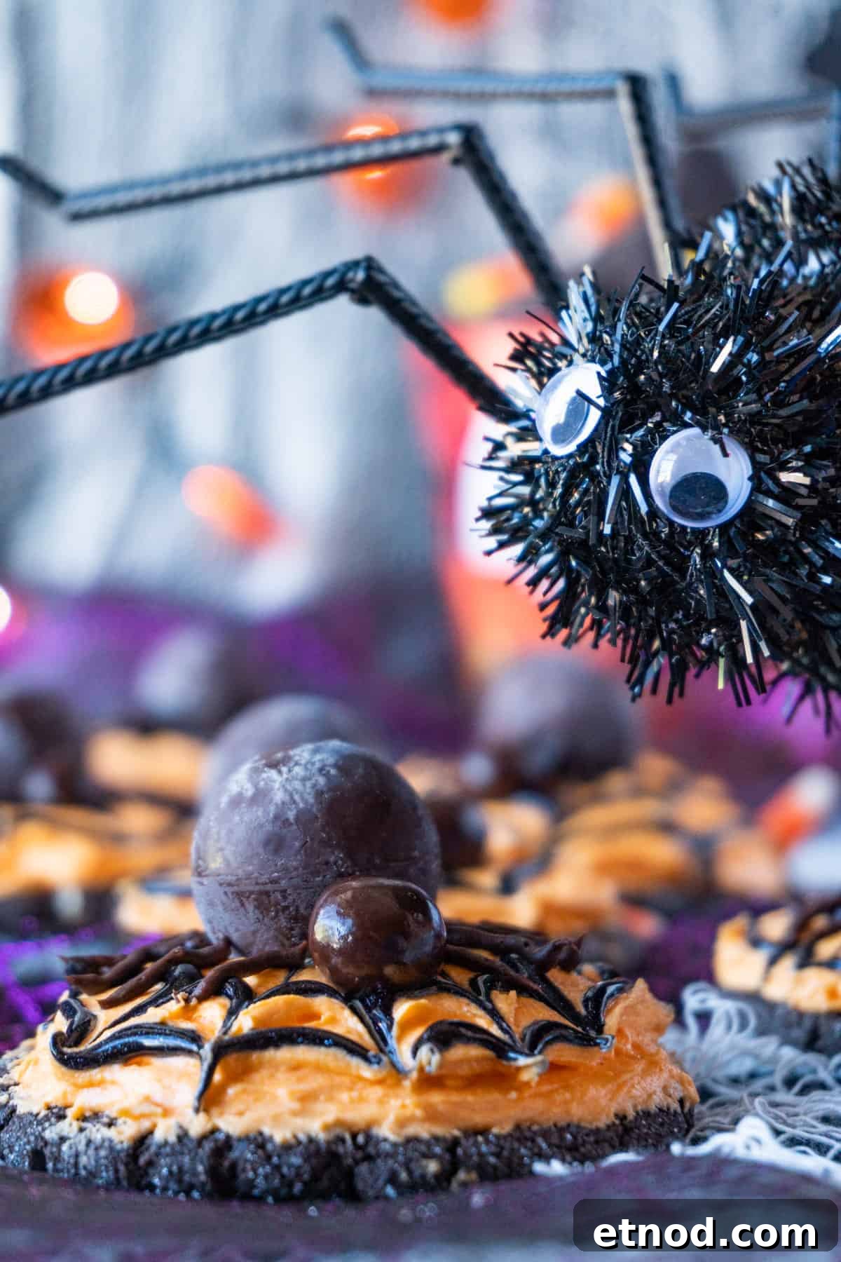 Halloween Spider Cookies, decorated with orange frosting and candy to form spider, with a large fake spider next to them.