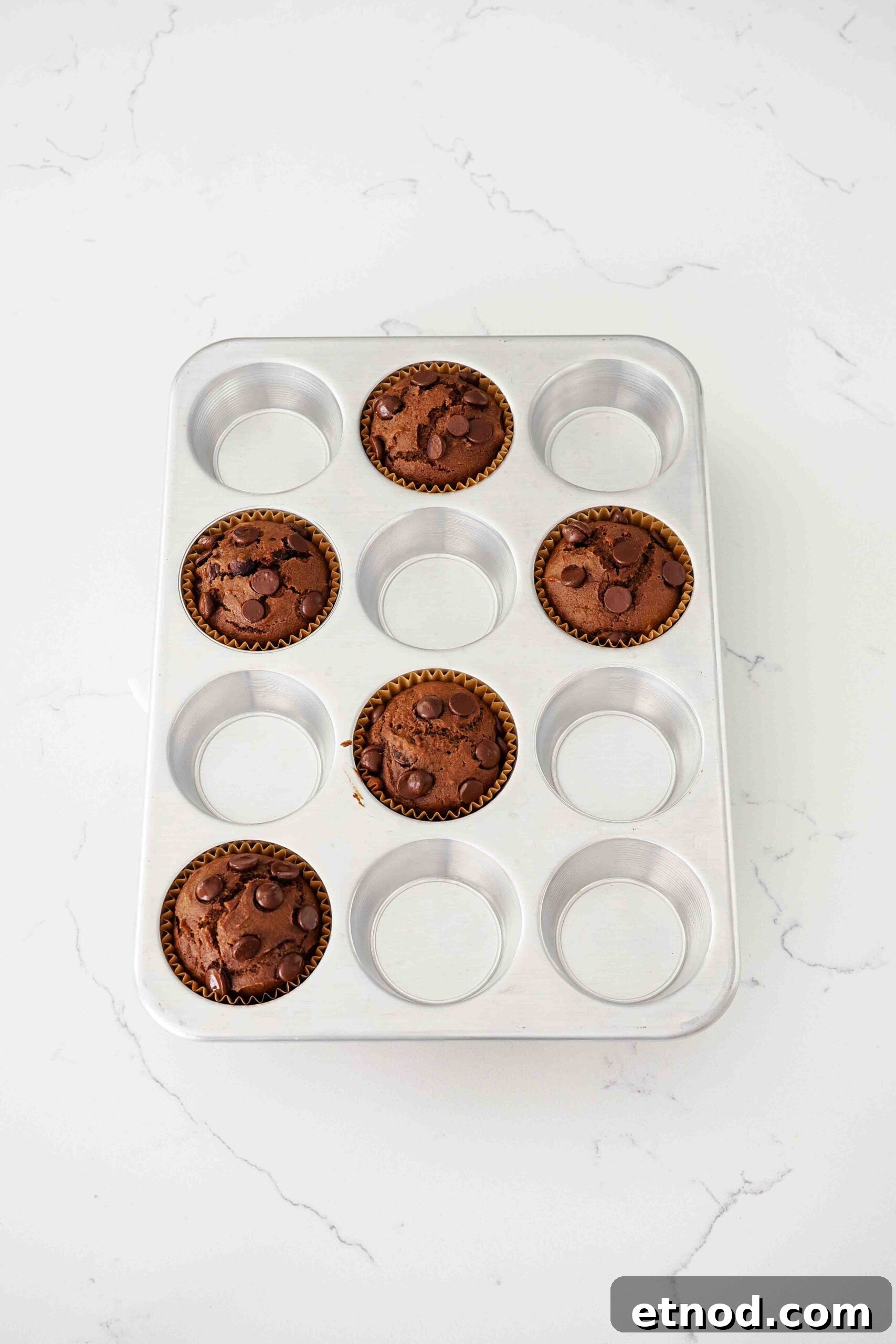Chocolate Pumpkin Muffins with Melty Chips — Fall Baking Recipe 11 Fully baked chocolate pumpkin muffins in an aluminum muffin pan.