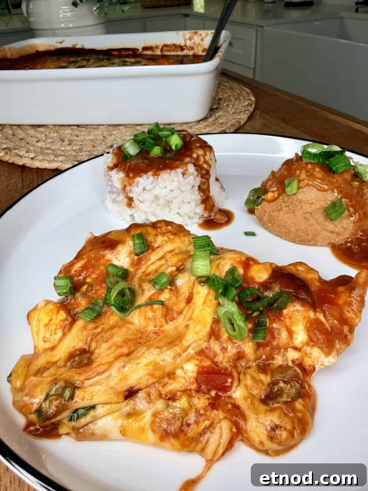 Creamy Baked Salsa Chicken Recipe for Weeknight Dinners 11 A plate with an omelet topped with sauce and chopped green onions, a serving of white rice with sauce, and a tofu puff garnished with green onions. A baking dish with more sauce is in the background.