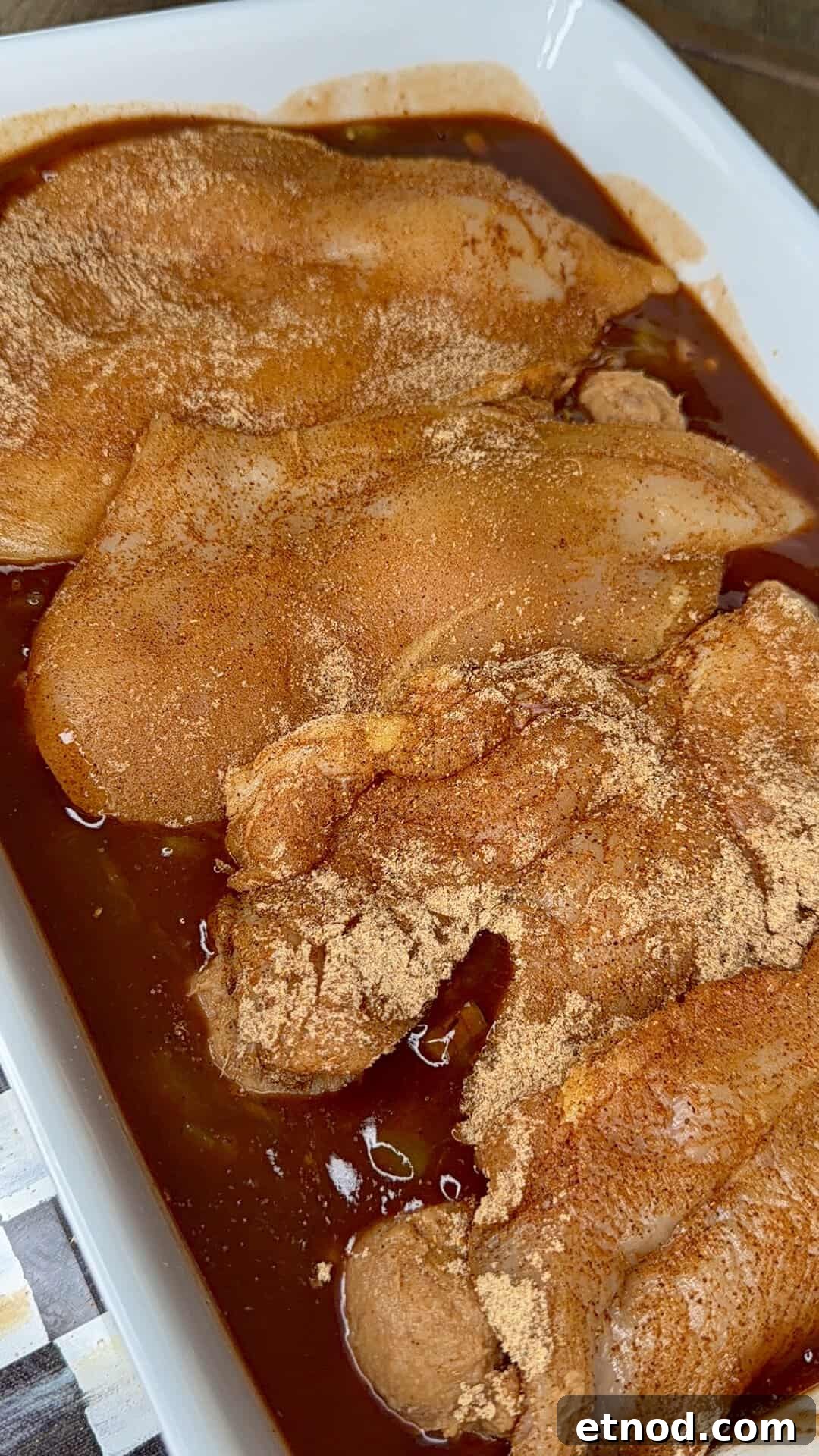 Creamy Baked Salsa Chicken Recipe for Weeknight Dinners 5 Raw chicken breasts coated with a reddish spice blend are marinating in a tray filled with a dark, seasoned liquid. The chicken is uncooked and evenly covered in spices and marinade.