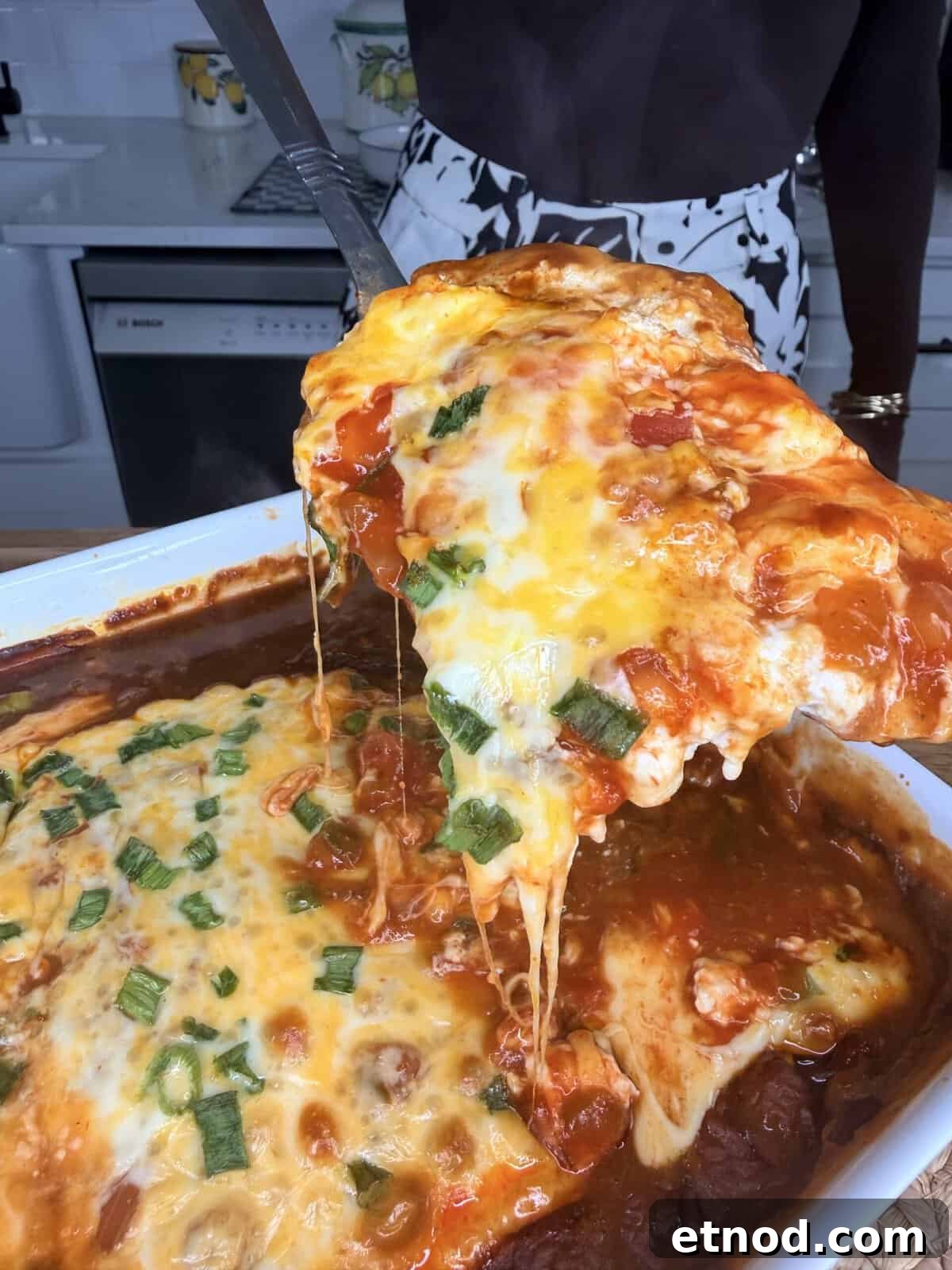 Creamy Baked Salsa Chicken Recipe for Weeknight Dinners 8 A person serves a cheesy, baked lasagna from a white dish; the lasagna is topped with melted cheese, tomato sauce, and chopped herbs, with cheese stretching as a slice is lifted.