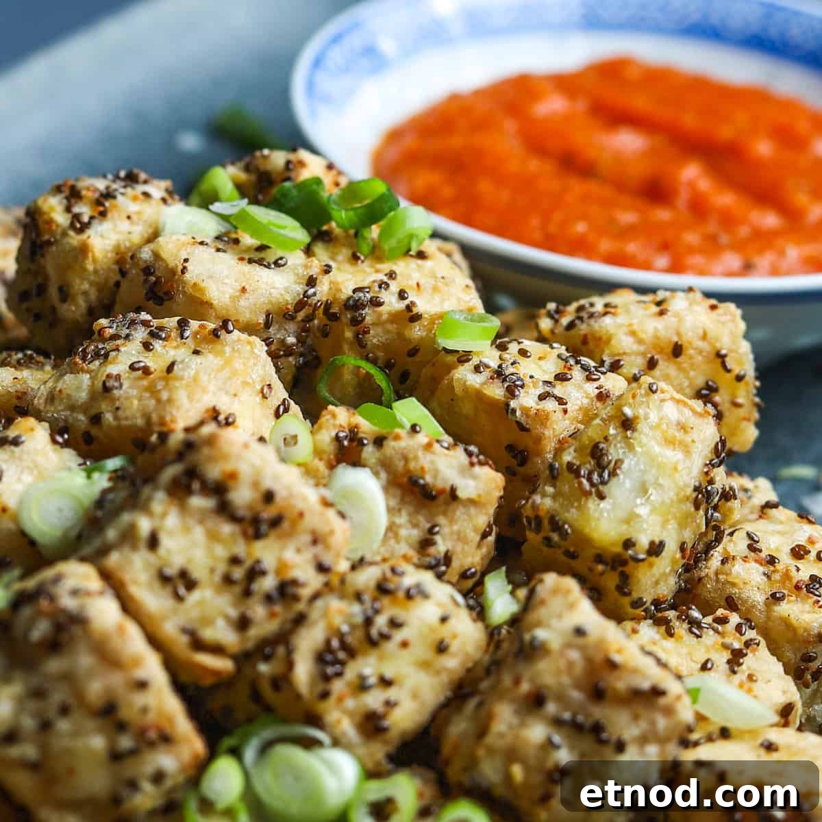 Crispy Air Fryer Tofu Coated with Chia Seeds for Extra Crunch 4 Close-up image showing crispy air fried tofu with sliced spring onions sprinkled on top and a bowl of kimchi sauce in the background.