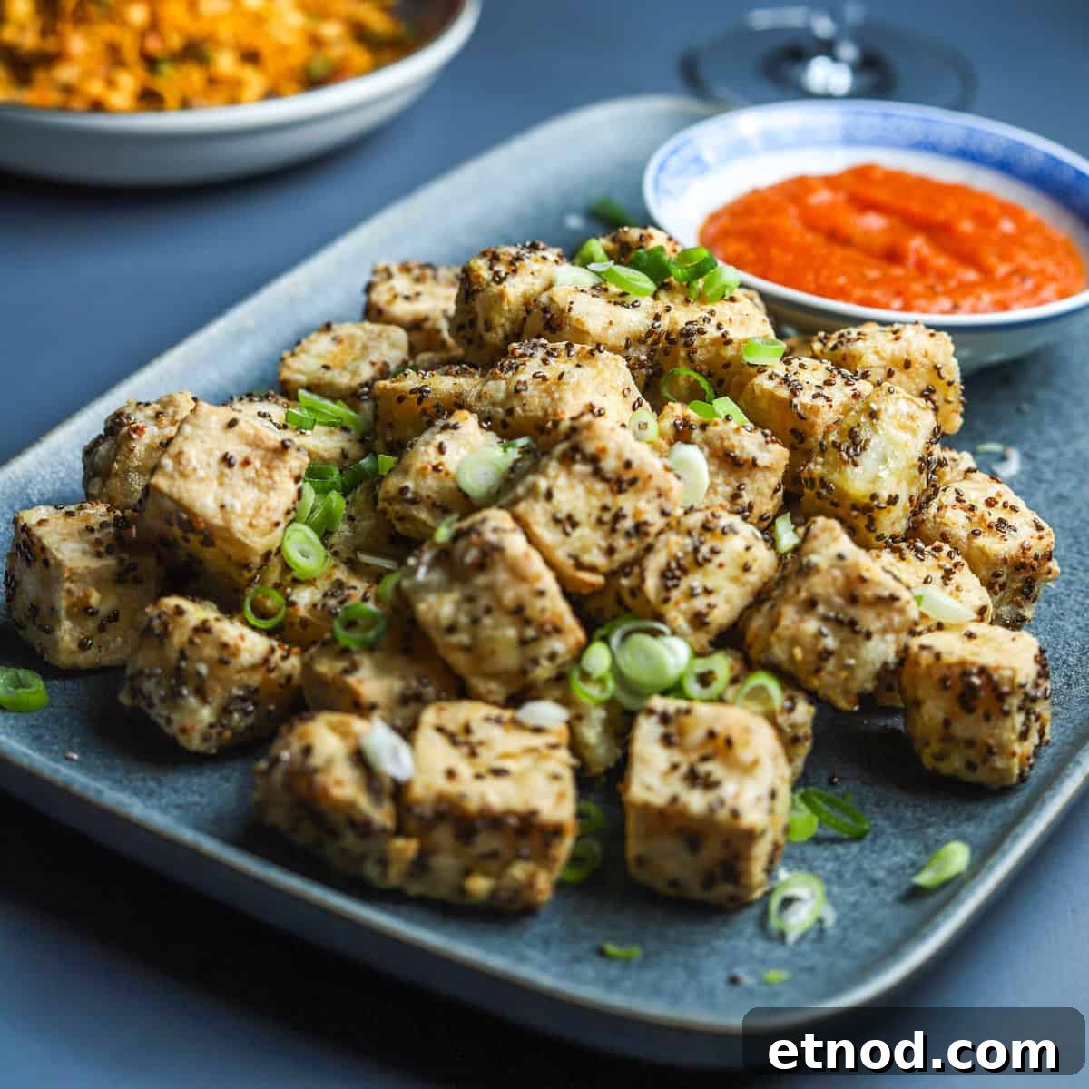 Crispy Air Fryer Tofu Coated with Chia Seeds for Extra Crunch 8 Blue grey plate filled with crispy chia tofu cubes sprinkled with sliced spring onions and served with a little bowl of kimchi sauce.