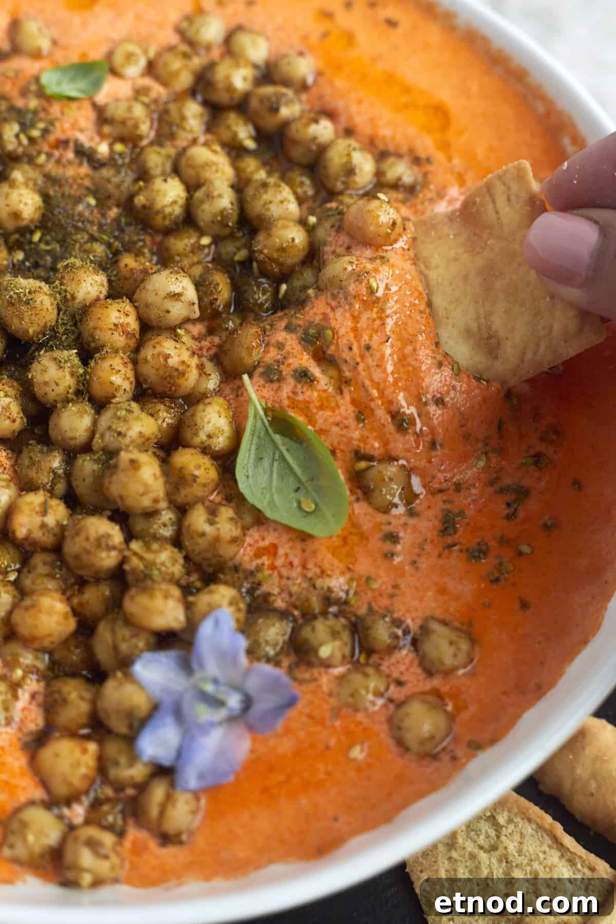 Roasted Red Pepper and Feta Dip with Crispy Chickpeas 4 a hand dipping a pita chip into a bowl of Roasted Red Pepper Feta Dip with Crispy Chickpeas