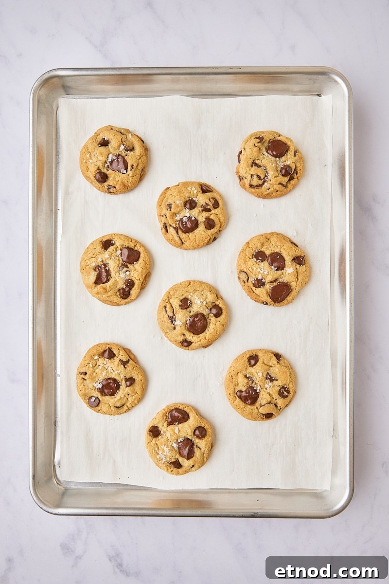 Brown Butter Chocolate Chip Cookies with Extra Chewiness 13 Baked cookies topped with flaky salt on parchment-lined baking sheet