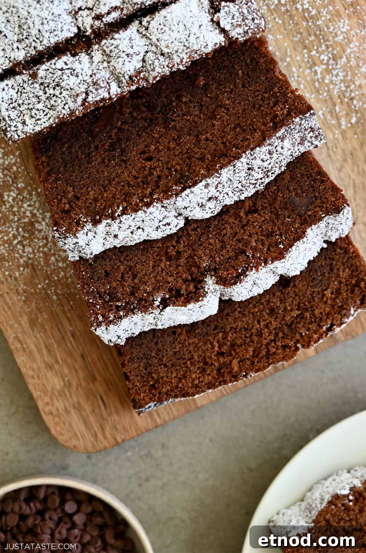Decadent Chocolate Loaf Cake Recipe for Moist, Rich Results 12 Thick slices of chocolate loaf cake dusted with powdered sugar on a wooden cutting board.