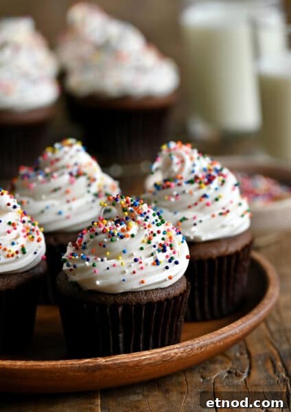 Decadent Chocolate Loaf Cake Recipe for Moist, Rich Results 14 Chocolate cupcakes topped with vanilla frosting and rainbow sprinkles on a wood serving plate.