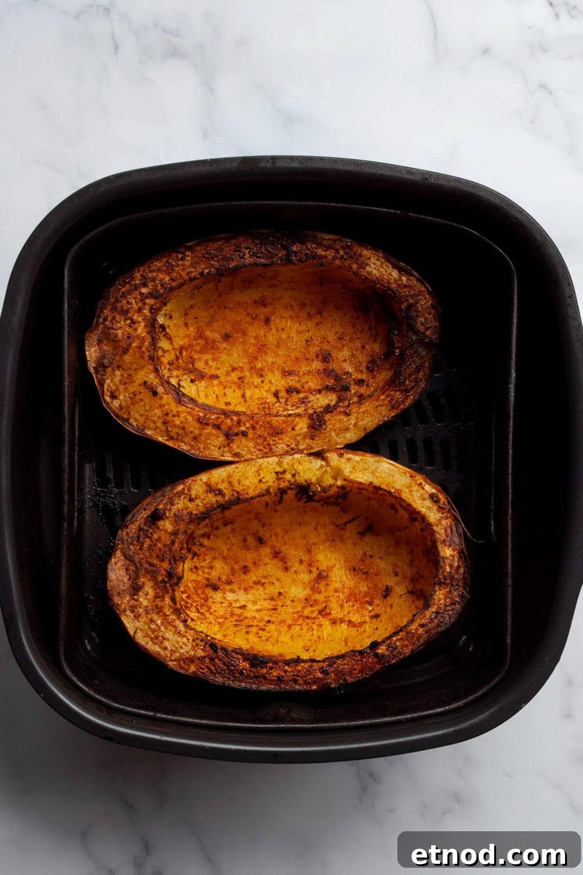 Crispy Air-Fried Spaghetti Squash Recipe 7 Two fork-tender, crispy cooked spaghetti squash halves sitting in an air fryer basket.