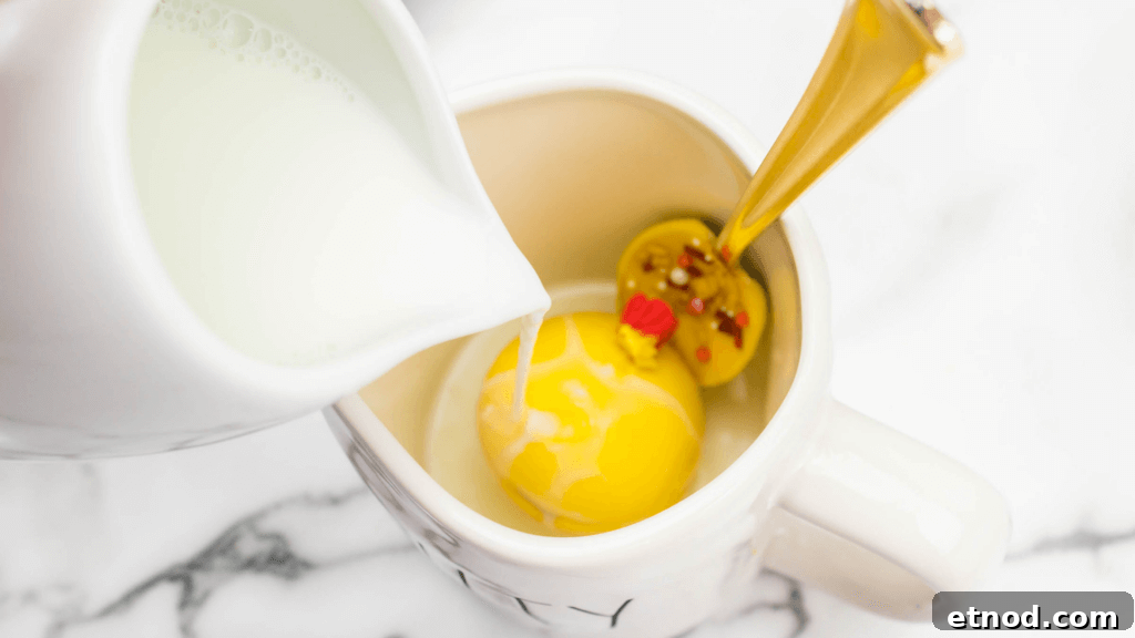Disney's Beauty and the Beast Chocolate Spoons: Step-by-Step Guide 6 Pouring hot milk onto a yellow hot cocoa bomb with a yellow Disney Inspired Beauty & the Beast Chocolate Spoons in a mug.