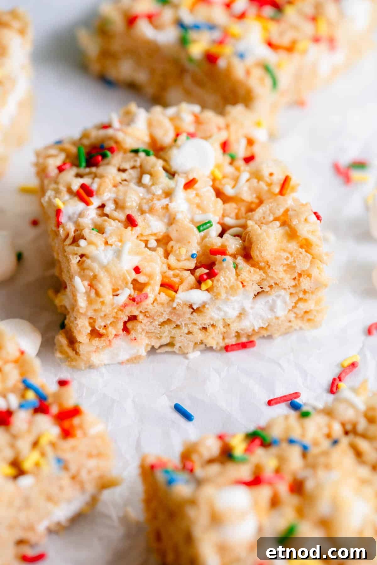 Birthday Cake Rice Krispie Treat on a piece of parchment paper with sprinkles scattered around it.
