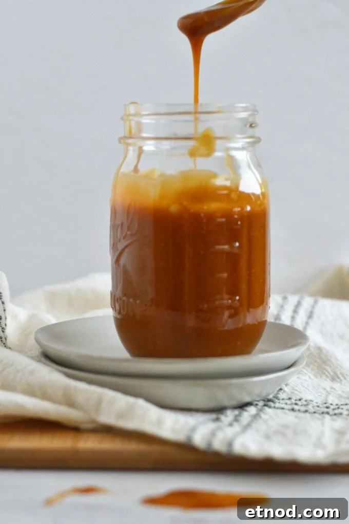 Creamy Cookie Butter Caramel Sauce Recipe 15 a spoonful of caramel sauce dripping into a mason jar.